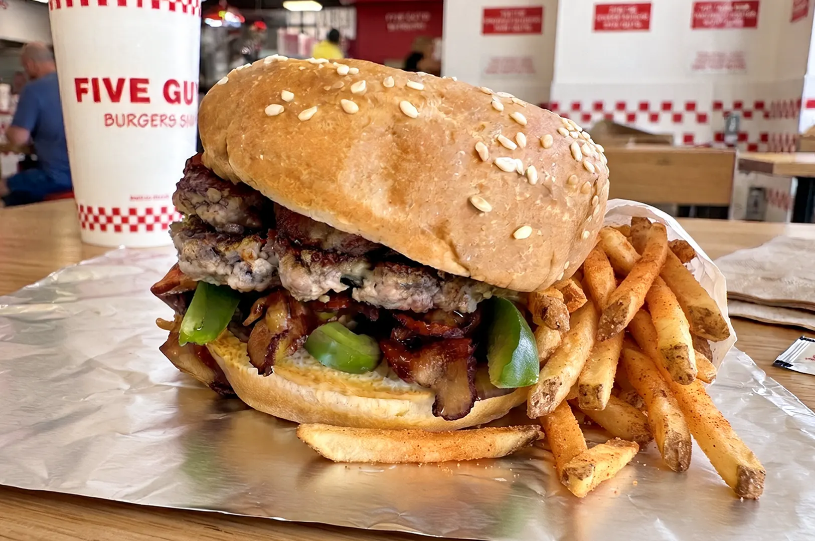 A Five Guys burger and seasoned french fries served on foil with a drink cup