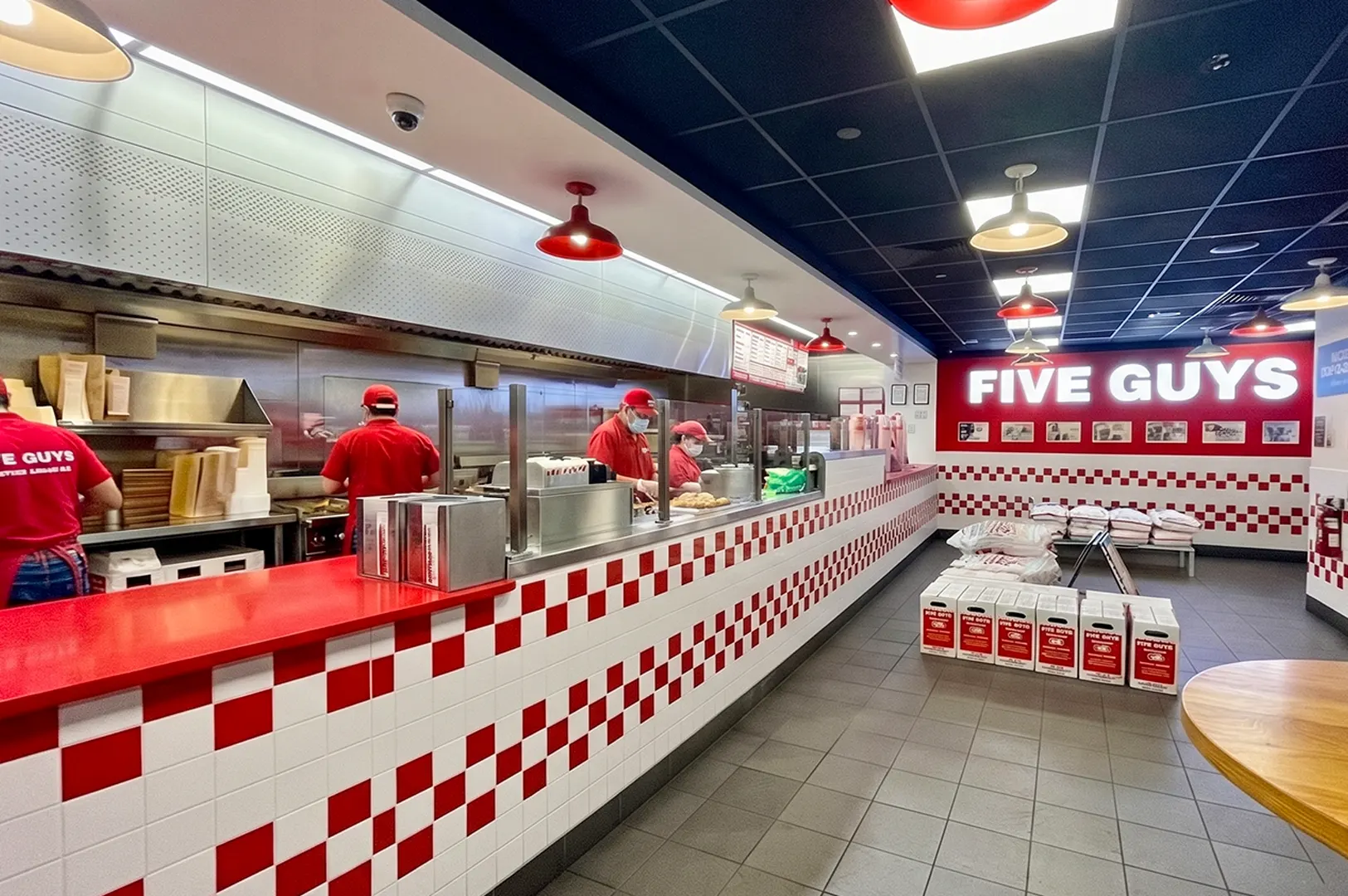 Inside view of a Five Guys restaurant showing the kitchen counter and red-and-white checkered interior.