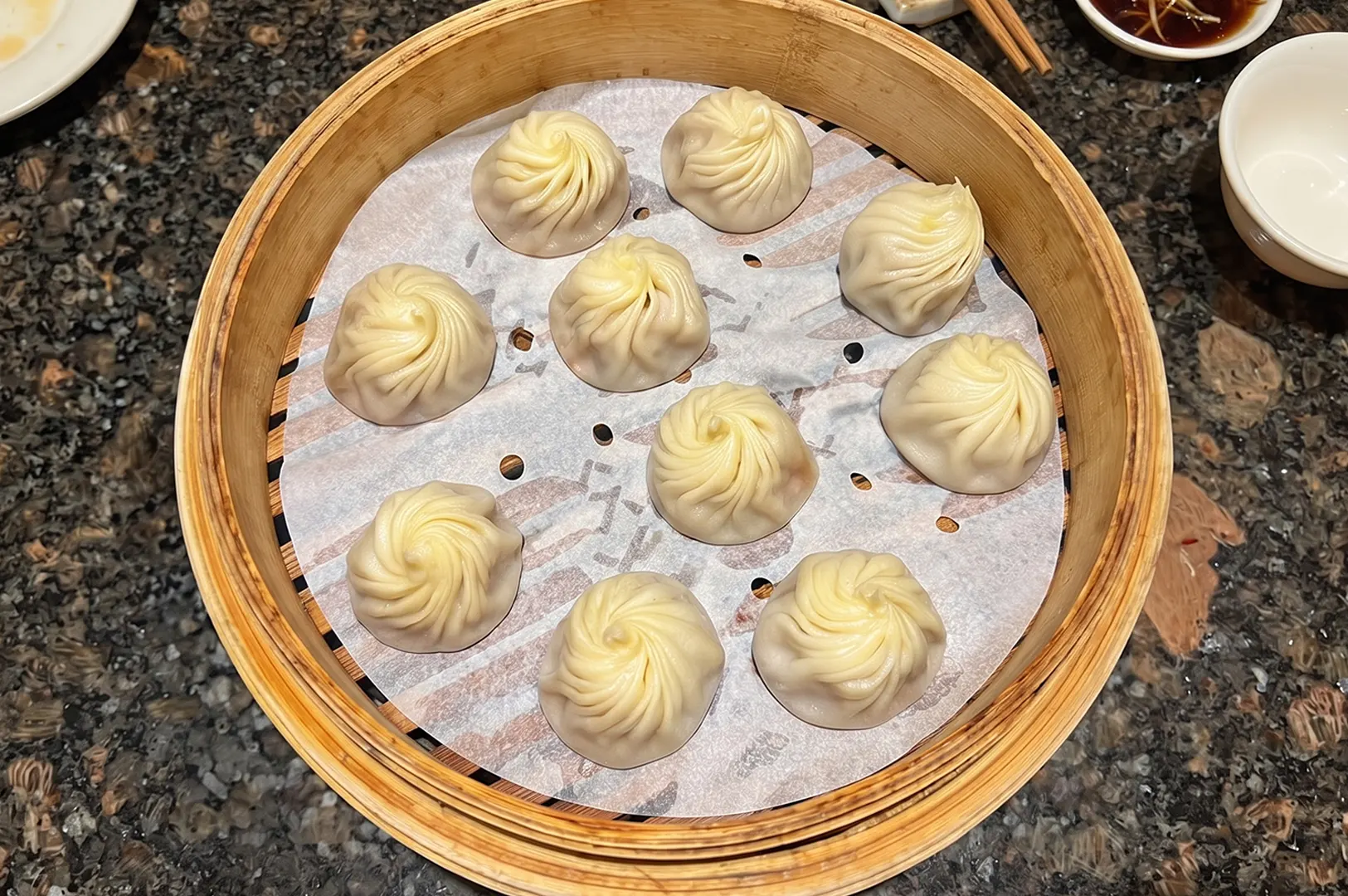 Freshly steamed Din Tai Fung xiao long bao soup dumplings in a bamboo basket.