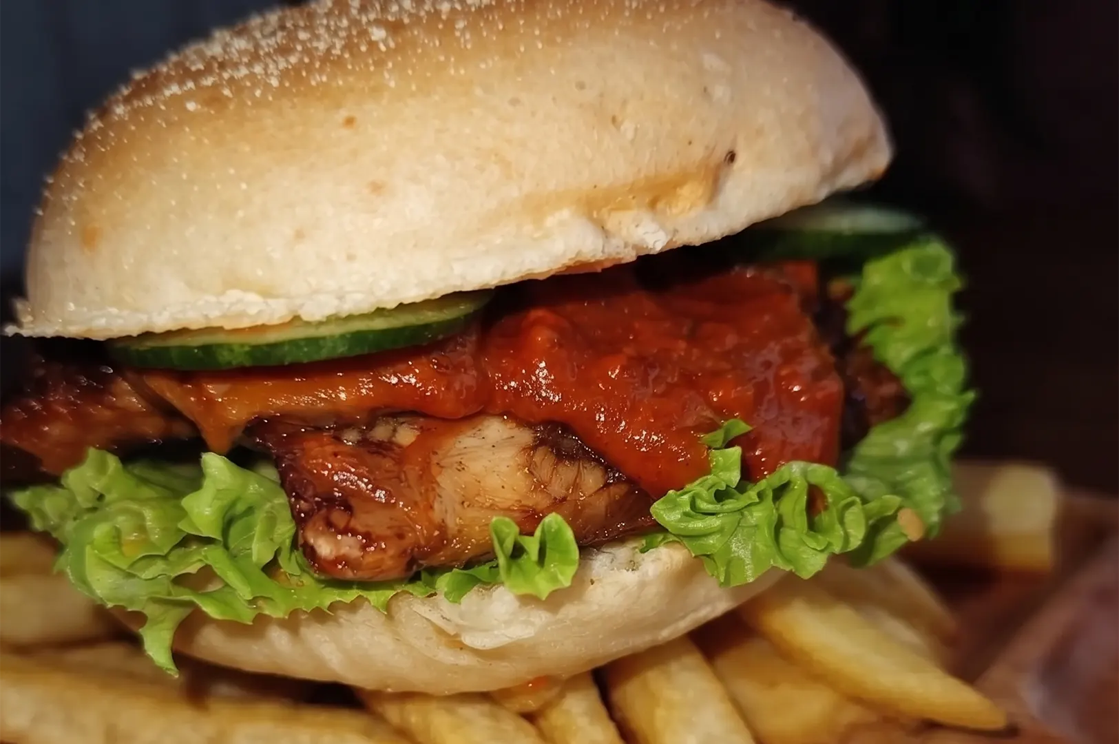 Delicious plant-based burger with sauce, lettuce, and cucumber served with fries.