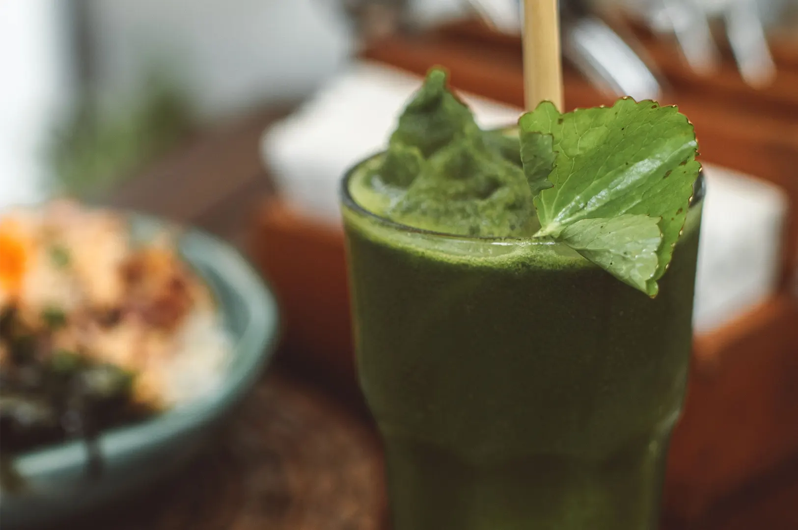 Close-up of a fresh organic green juice or smoothie in a glass with a bamboo straw and leafy garnish.