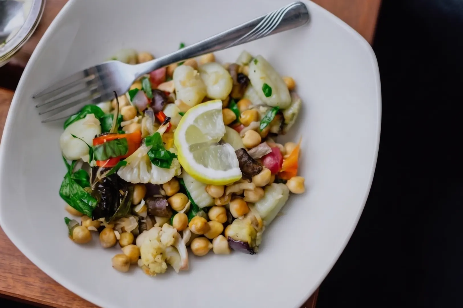 A bowl of vegan meal with chickpeas, vegetables, and a lemon slice.