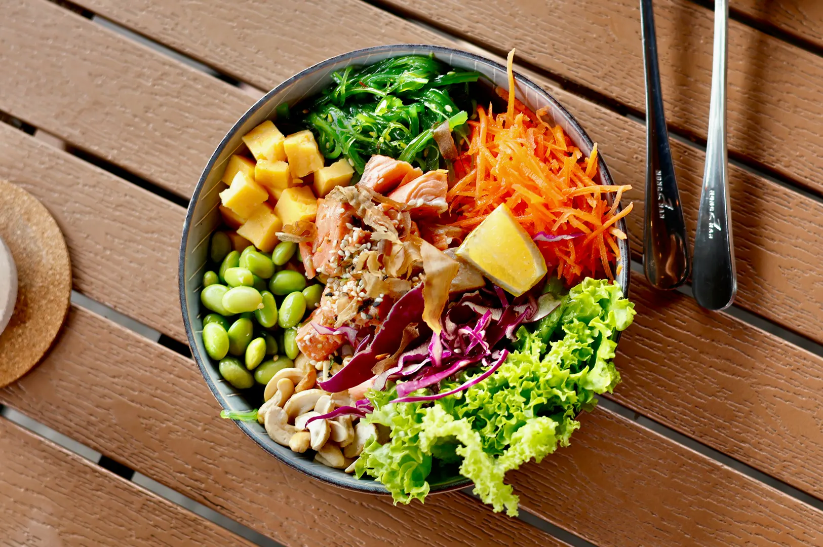 Colorful plant-based meal bowl with fresh vegetables, edamame, and greens on a wooden table.