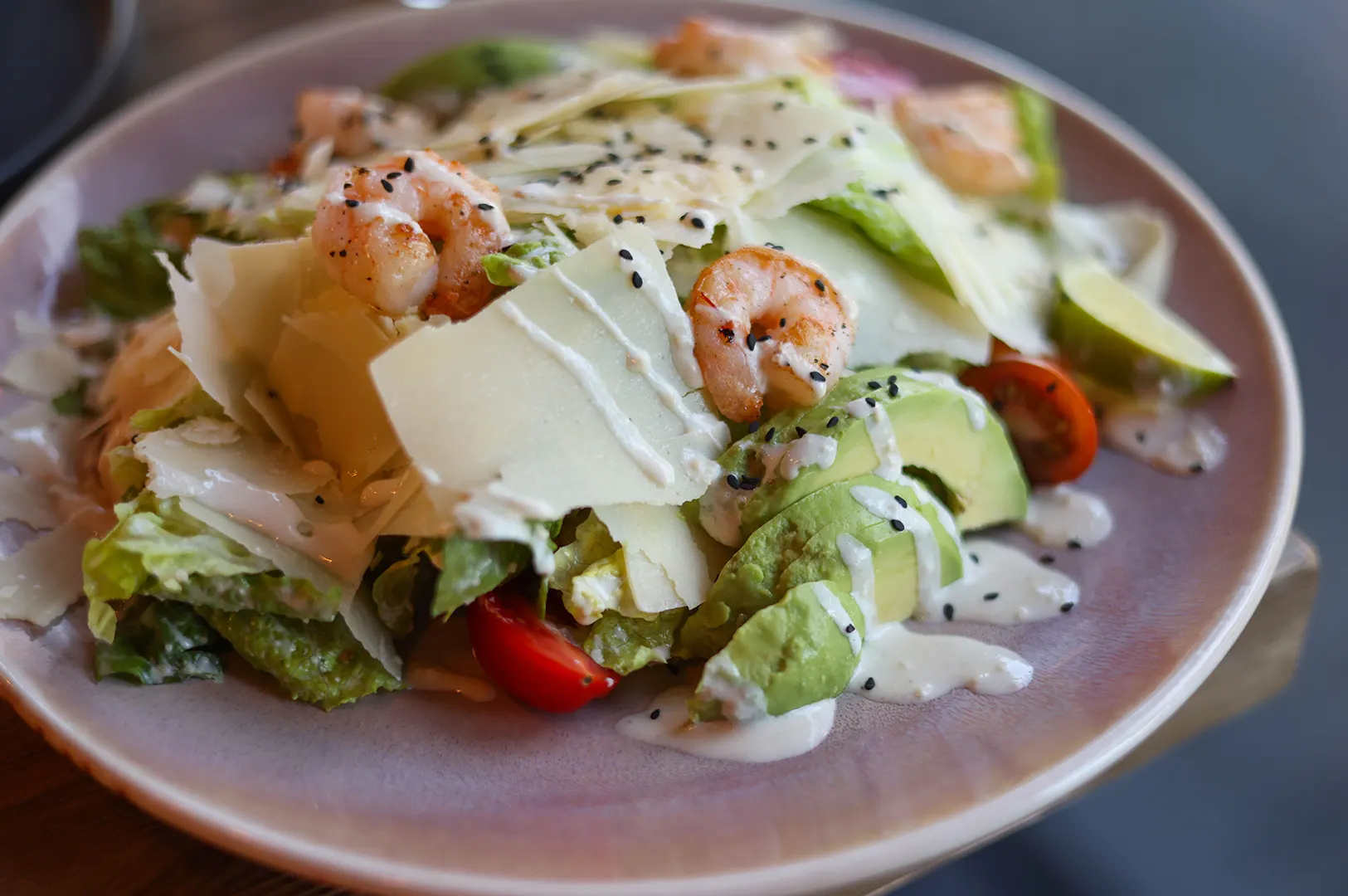 A rich salad bowl topped with shrimp, avocado slices, cheese, and creamy dressing, illustrating how toppings and dressings impact the nutritional value of a menu choice.