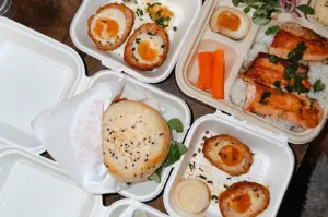 Assorted healthy meal prep delivery containers with salmon, scotch eggs, and a burger in Singapore.