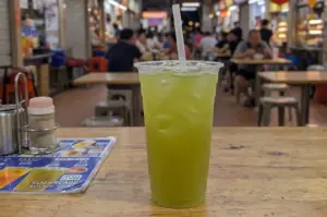 Fresh iced sugarcane juice in a clear plastic cup on a wooden table at a Singapore hawker centre.