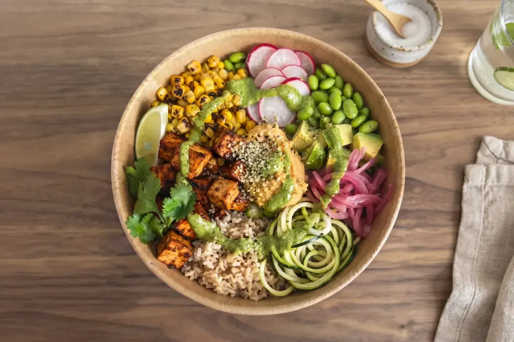 Close-up of a customizable vegetarian bowl with assorted toppings including tofu, corn, edamame, and zucchini noodles.