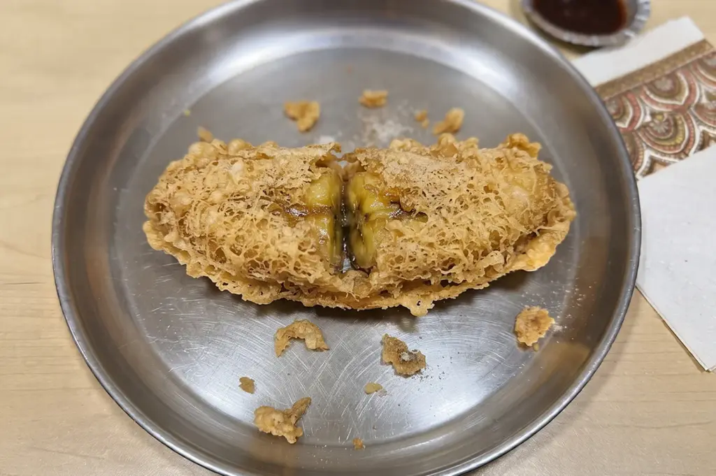 A freshly fried banana fritter, or goreng pisang, cut in half on a metal plate.
