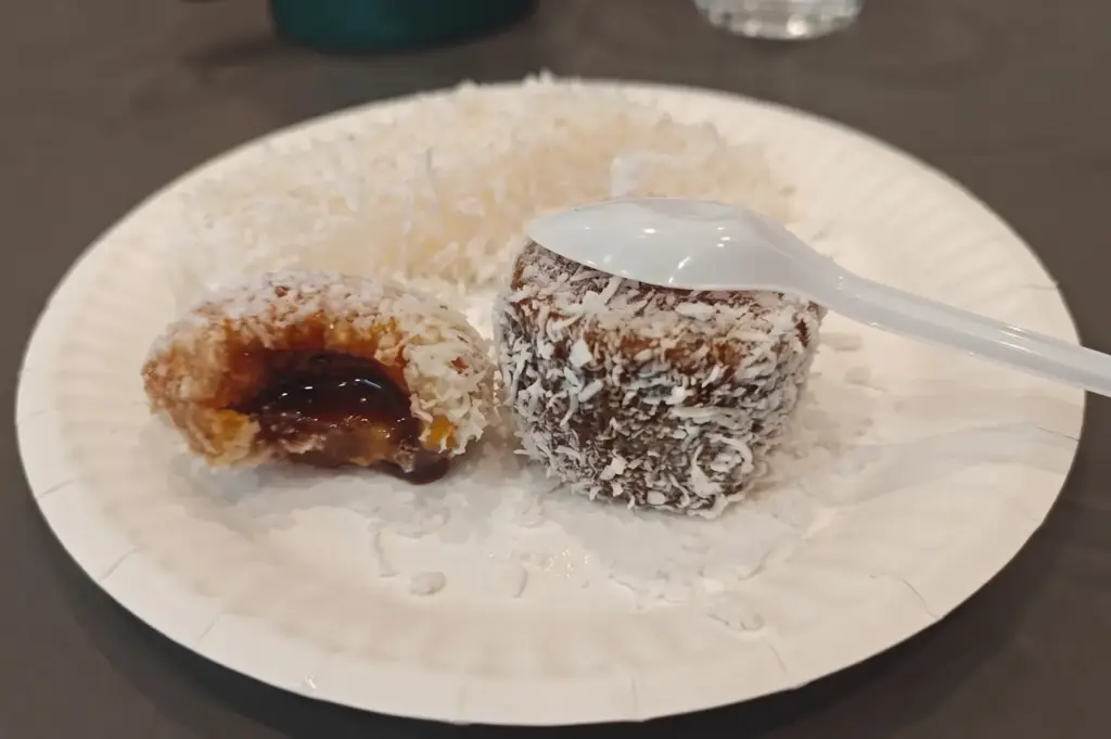 Two pieces of traditional tapioca cake coated in grated coconut on a white paper plate, with one piece cut open revealing a sweet filling.