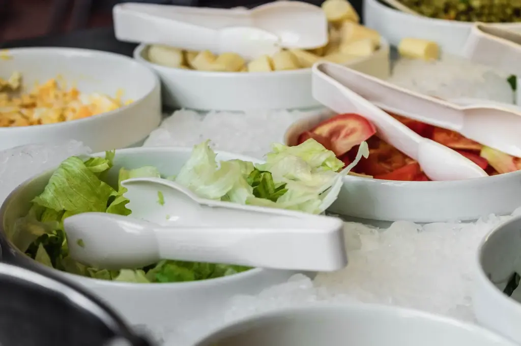 A fresh salad bar station with separate bowls of lettuce, tomatoes, and other ingredients, representing custom food choices and meal components.