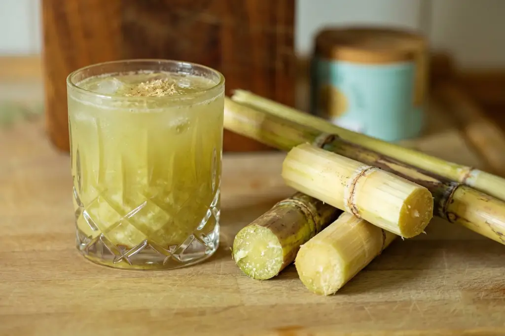 Fresh sugarcane juice with ice and natural sugarcane stalks on a wooden cutting board.