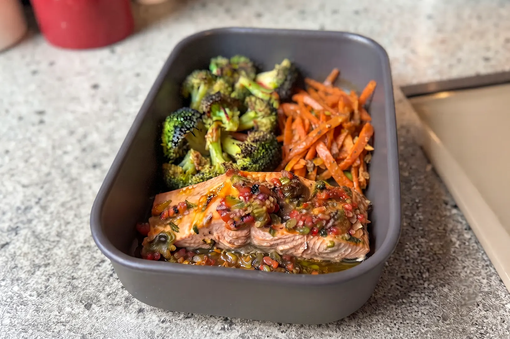 Close-up of Prepped Singapore Ginger Miso Salmon meal kit in a container, featuring a glazed salmon fillet, roasted broccoli, and carrots.