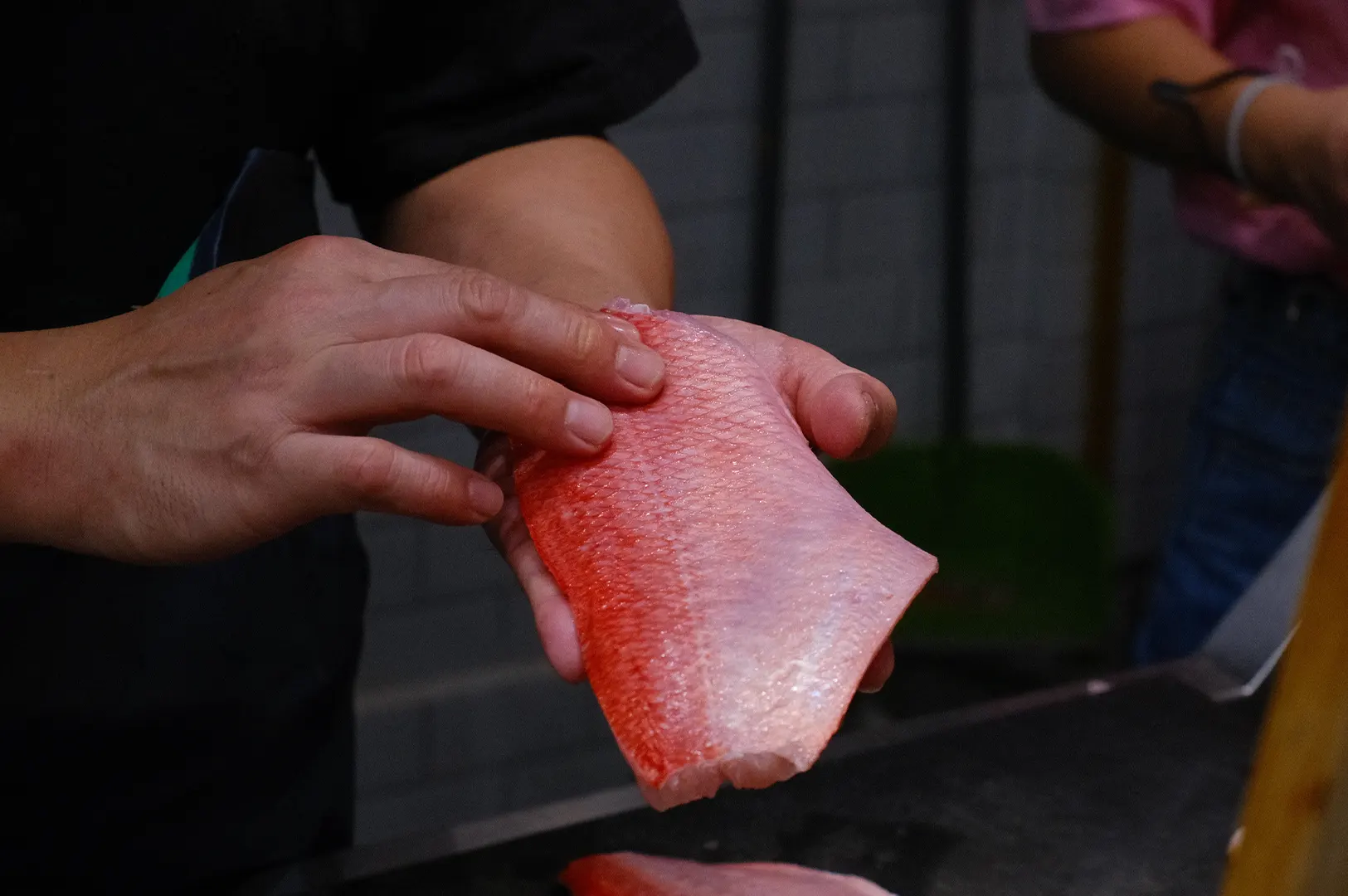 Person holding a fresh slice of raw fish for sashimi preparation.