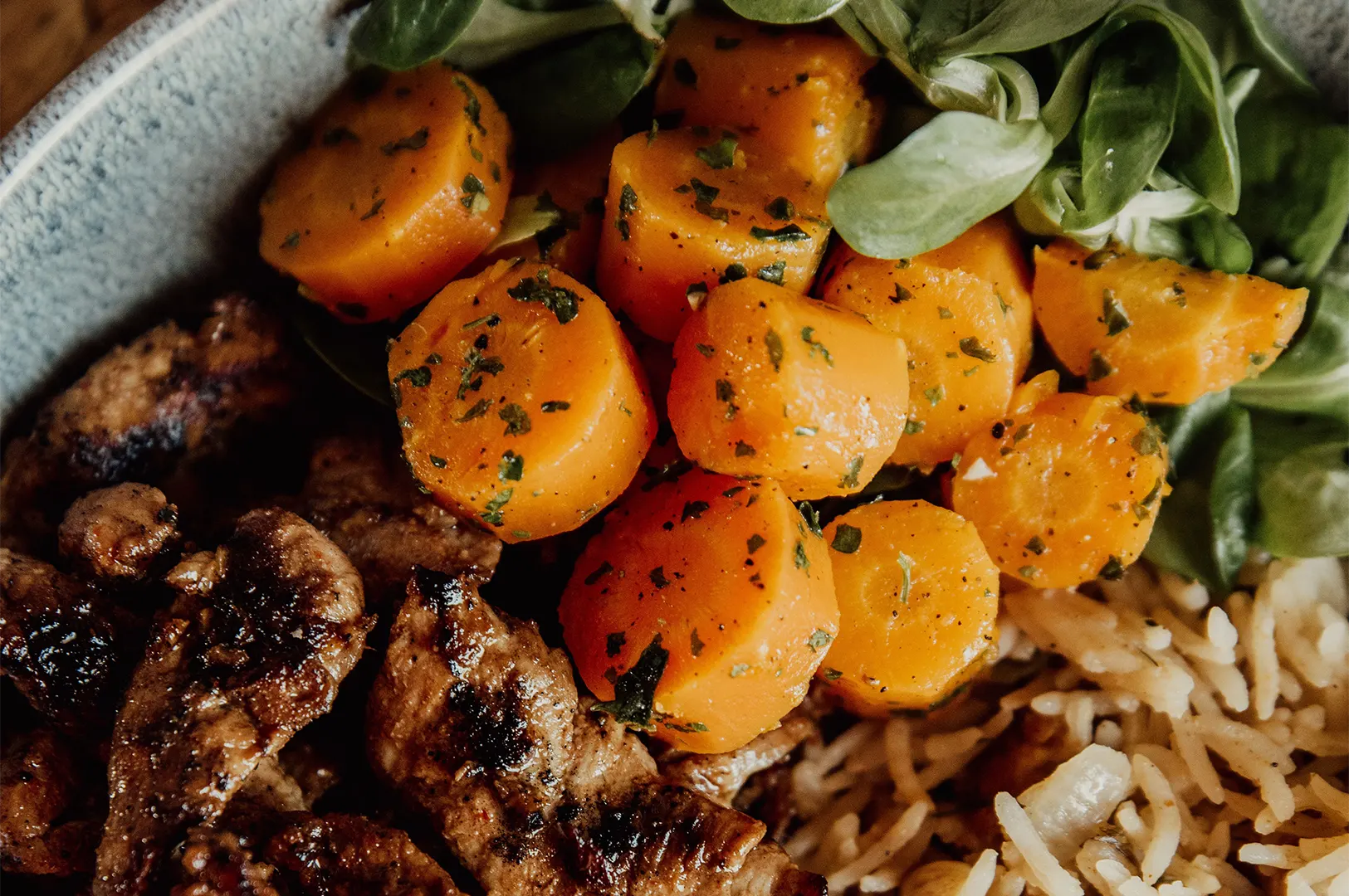 Close up of a reheated YoloFoods SG meal featuring sliced carrots, grilled meat, rice, and fresh greens.