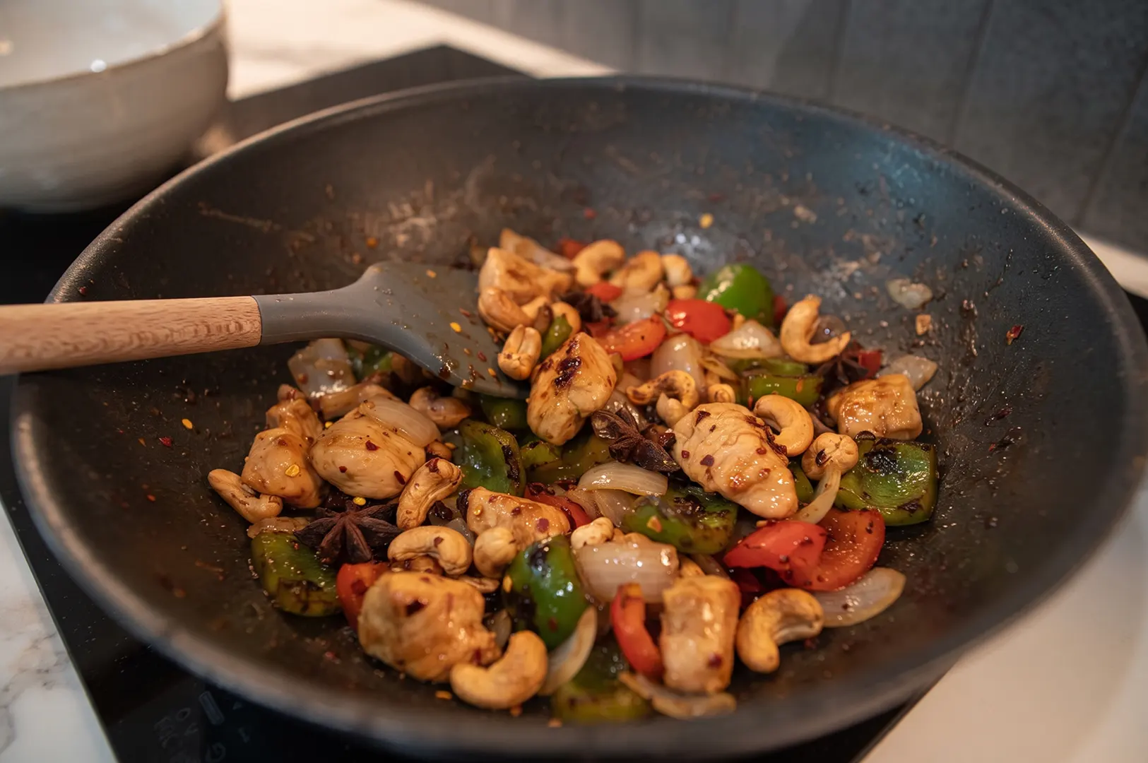 Prepped Singapore meal kit chicken and cashew nuts stir fry cooking in a wok with fresh vegetables and a spatula.