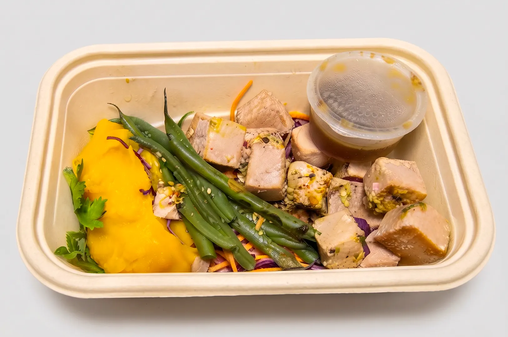TSquared Eats healthy meal prep box with chicken, green beans, and side sauce in a delivery container.