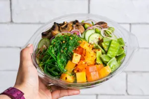 A person holding a healthy ready-to-eat frozen meal bowl with vegetables, tofu, and mushrooms.