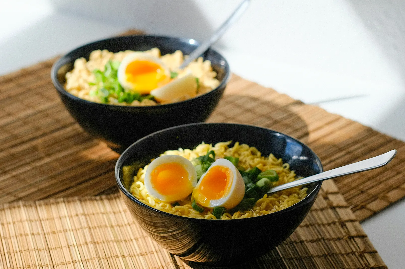 Upgraded instant noodles in a black bowl topped with a soft-boiled egg and green onions for a quick girl dinner.
