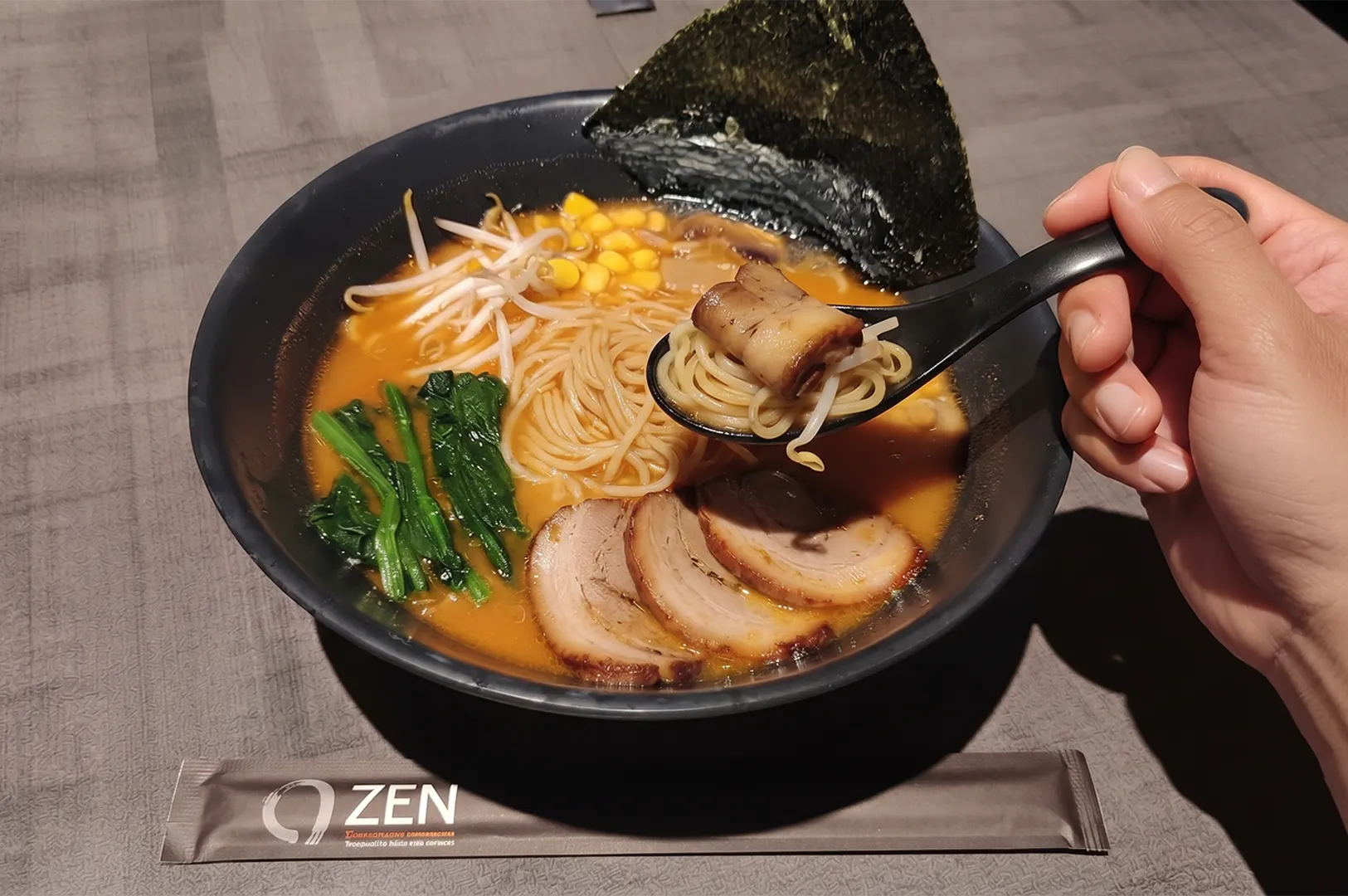 Bowl of Japanese ramen with noodles, chashu pork, and toppings on a dark table.