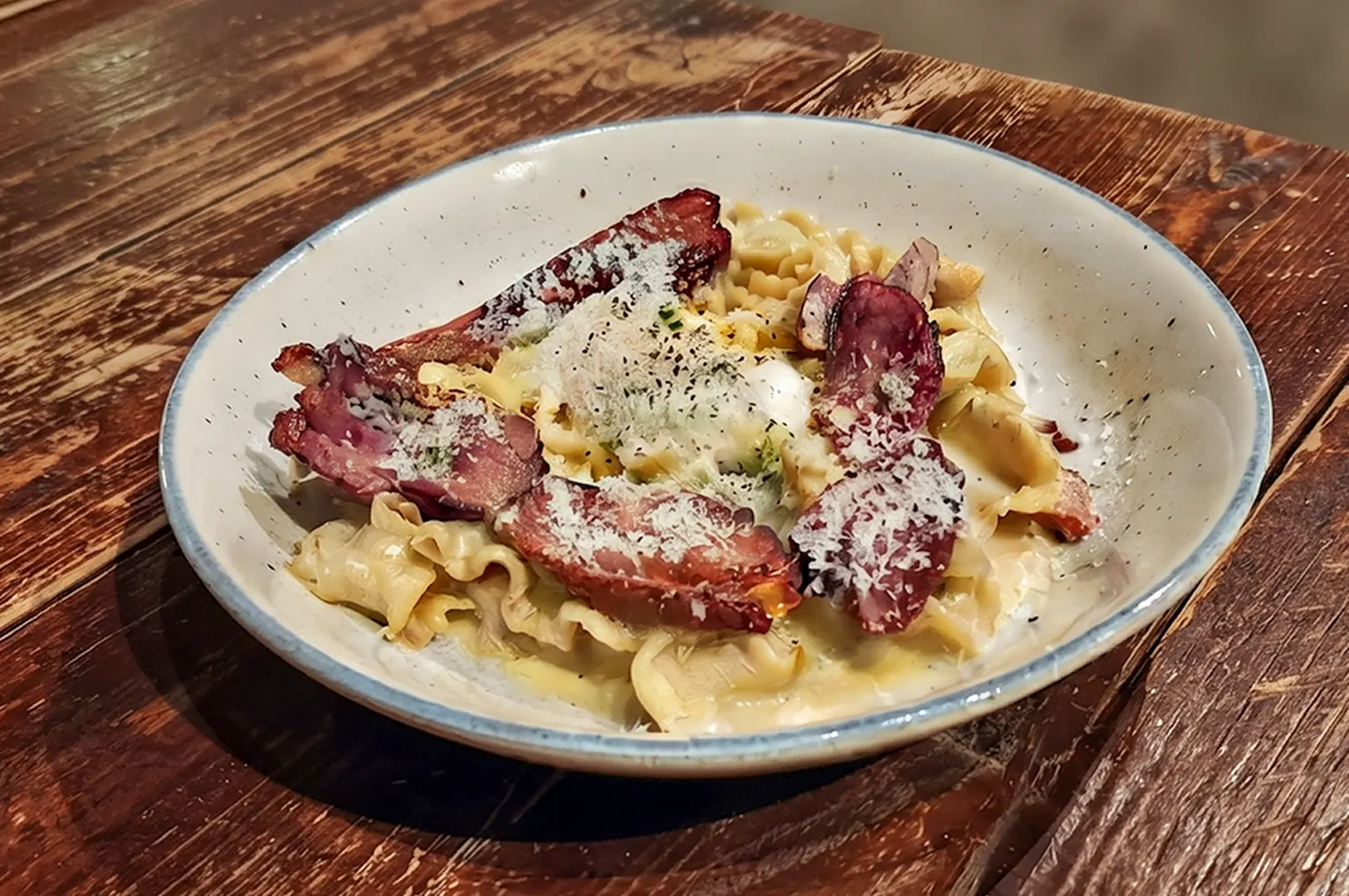 Classy carbonara pasta with smoked duck and egg served on a wooden table.