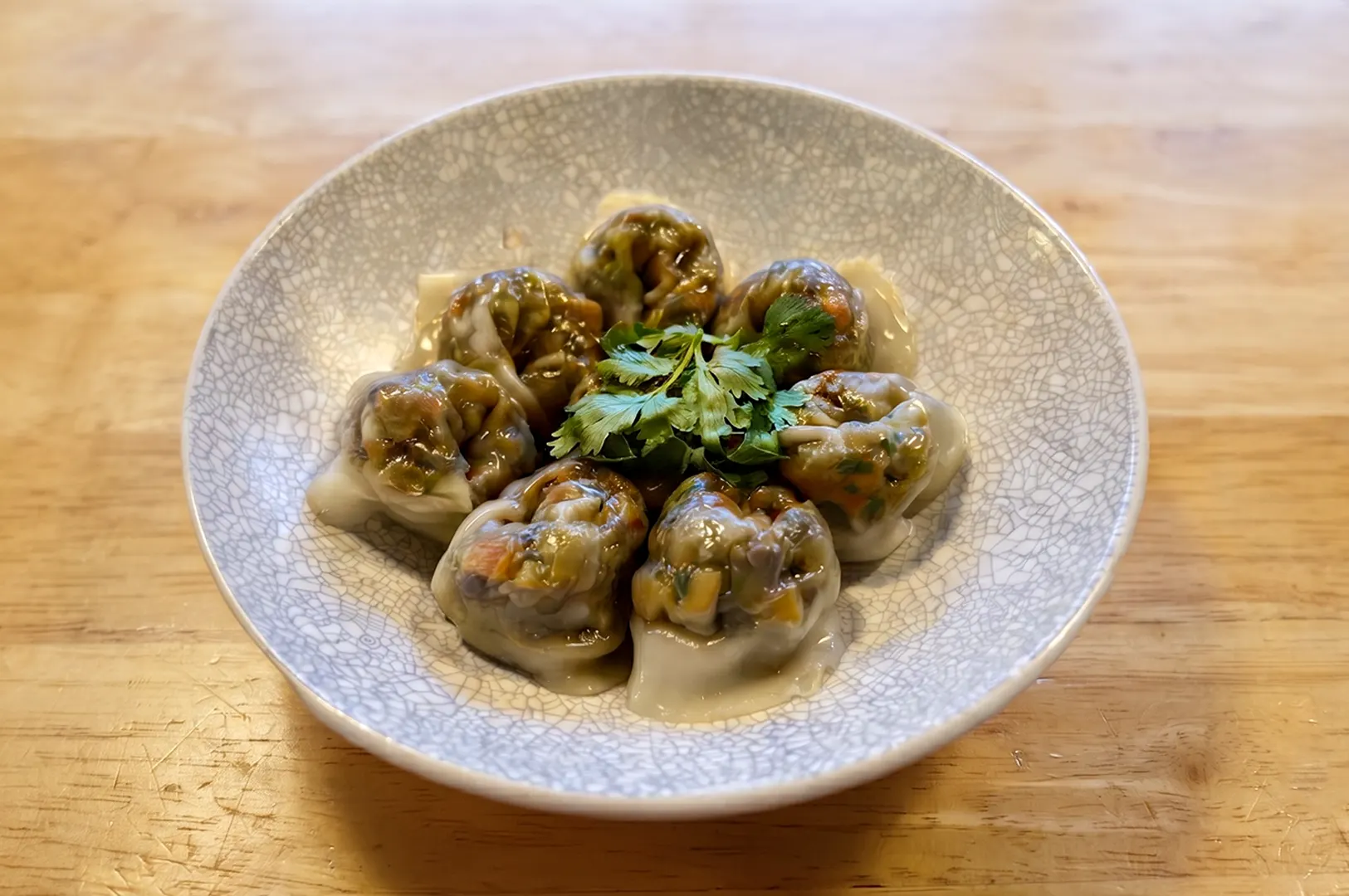Close-up of handmade steamed vegetable dumplings served in a grey bowl.