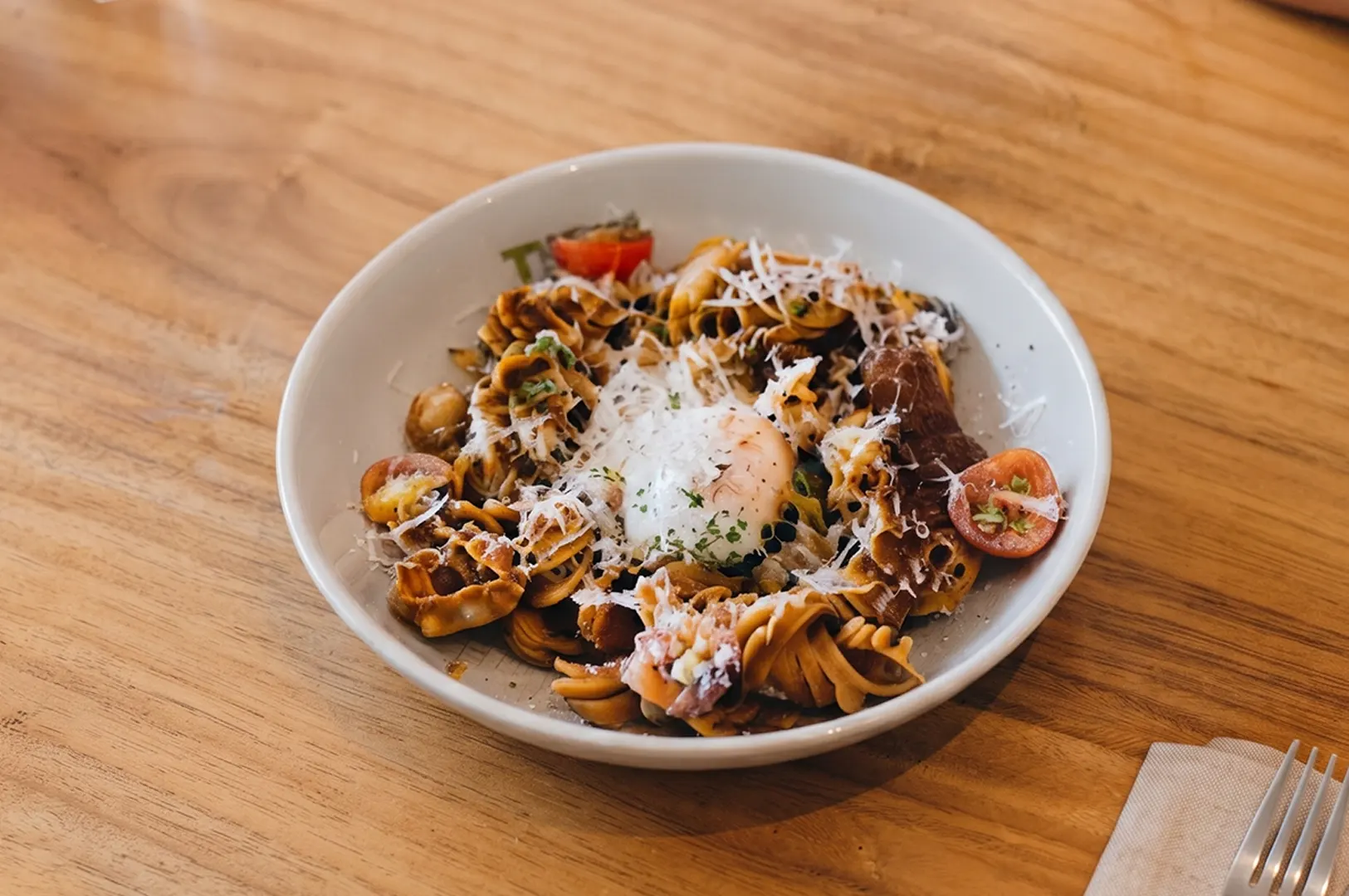Plate of Royal Ragu pasta with shredded beef, cherry tomatoes, and Grana Padano cheese on a wooden table.