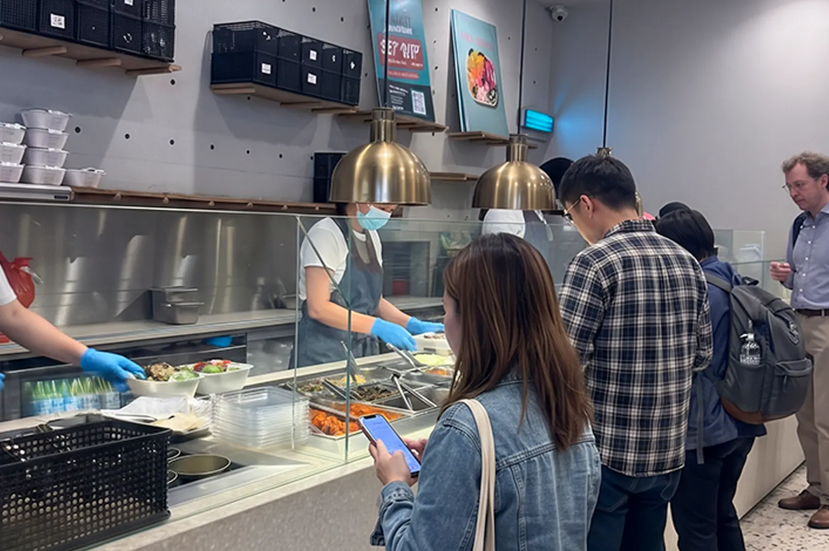 Customers queuing at a cafe order counter during lunch rush.