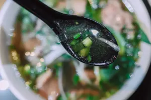 Close-up of a spoon scooping clear warm broth with spring onions for a comforting reset meal.