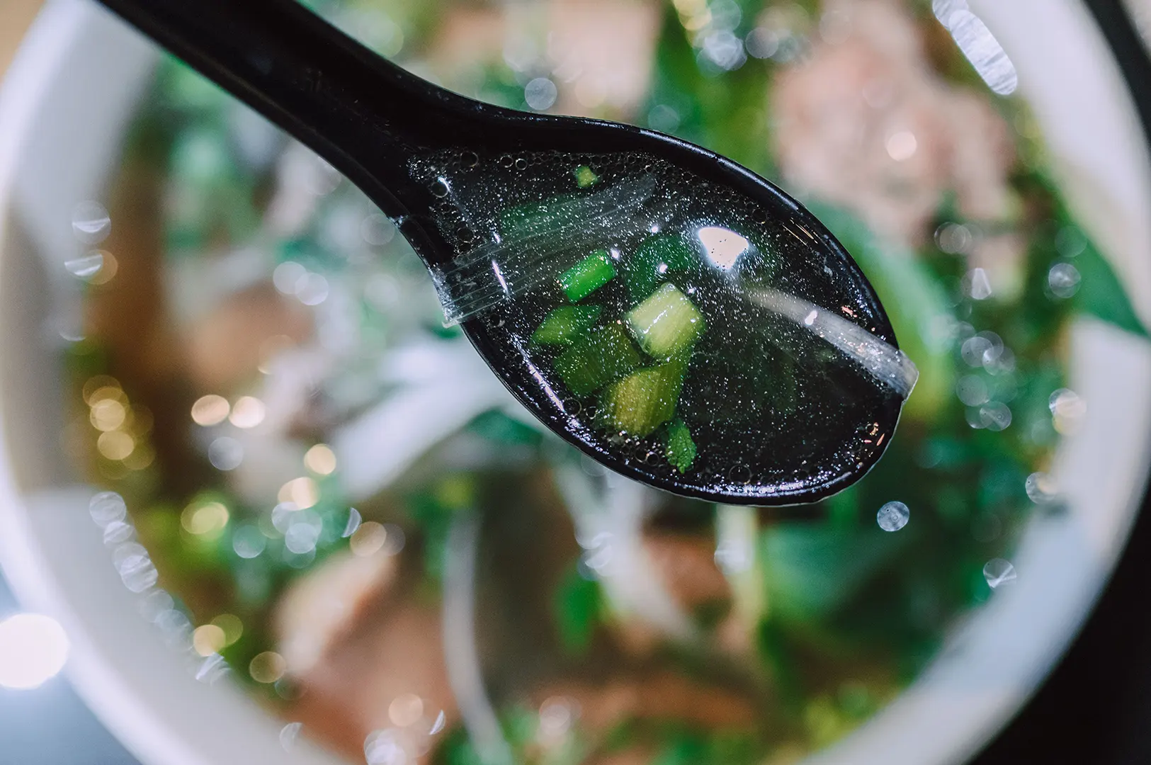 Close-up of a spoon scooping clear warm broth with spring onions for a comforting reset meal.